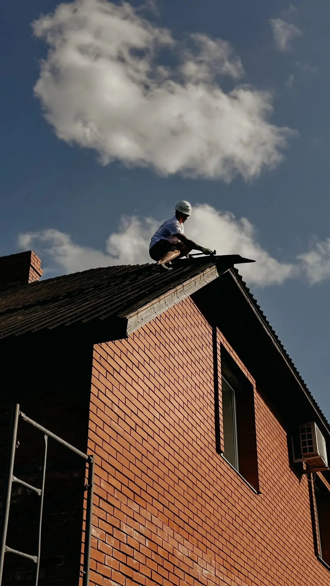 Un couvreur, de loin, accroupi sur le faîtage d'une maison en briques