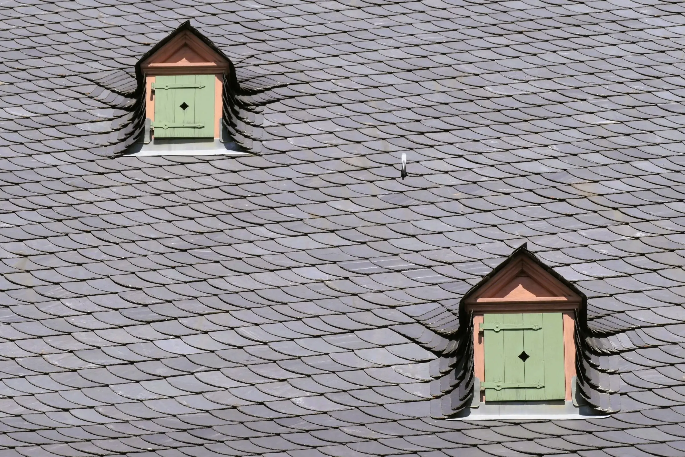 Un toit d'ardoise percé de deux lucarnes aux volets verts